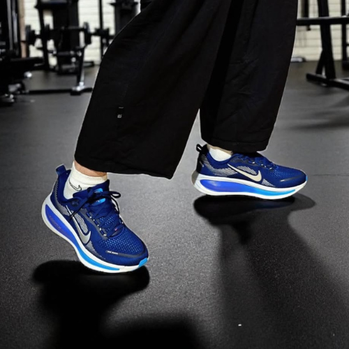 Person wearing blue athletic shoes with a brand logo on a dark floor.