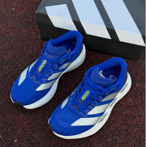 Blue sneakers with white stripes on a dark surface, Adidas box in the background