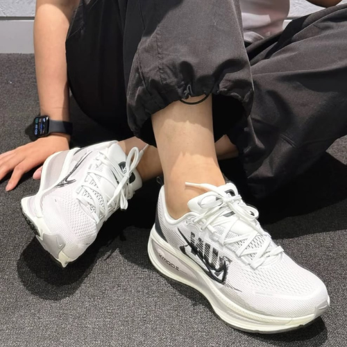 White sneakers with black accents worn by a person sitting on a gray floor.