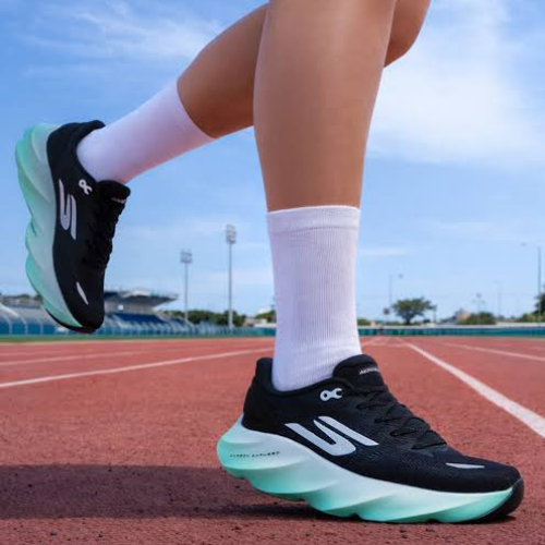 Person wearing black and green running shoes on a track with a clear blue sky.